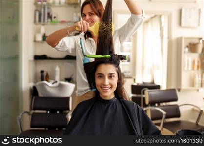 Hairdresser curls and combs woman&rsquo;s hair, hairdressing salon. Stylist and client in hairsalon. Beauty business, professional service. Hairdresser curls and combs woman&rsquo;s hair