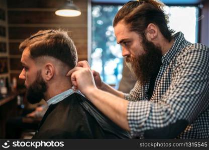 Hairdresser cutting hairstyle of the client man in black salon cape, barbershop on background