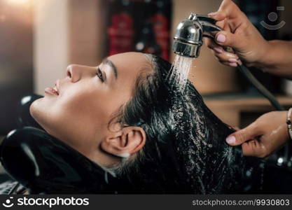 Hairdresser rinsing woman’s long black hair in hair salon. Young Woman Having Hair Washed in Salon