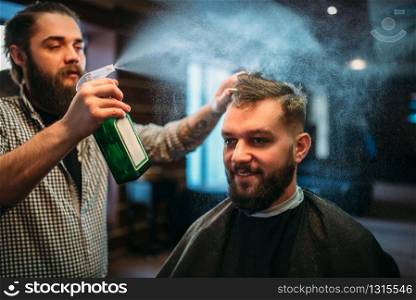 Hairdresser water with spray hair of the client man in black salon cape. Male person visit barbershop