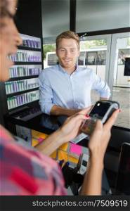 hairdresser with male client paying over electronic reader at counter