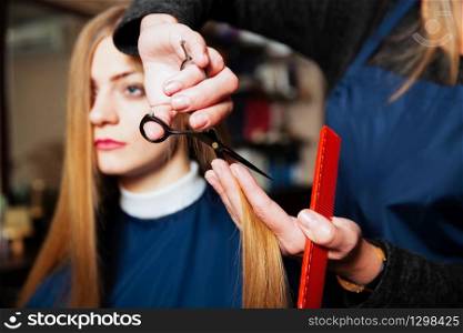 Hairdresser with scissors and comb cute hair to young woman.