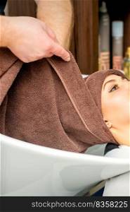 Hairdresser wraps female customer head with a towel in the sink at a hair salon. Hairdresser wraps female customer head