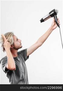 Hairstyle and fashion. Young trendy male hairstylist barber with new idea of look changing. Blonde man holding hair dryer and comb creating new hairdo. Young man drying hair with hairdryer