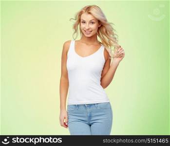 hairstyle, fashion and people concept - happy smiling beautiful young woman in white top and jeans with blonde hair over green background. happy smiling young woman with blonde hair