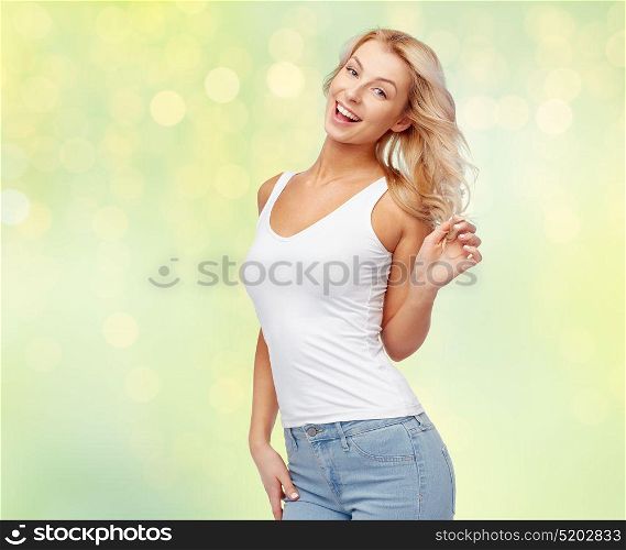 hairstyle, fashion and people concept - happy smiling beautiful young woman in white top and jeans with blonde hair over summer green lights background. happy smiling young woman with blonde hair