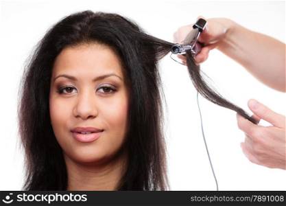 Hairstyling. attractive mixed race woman with long hair making hairstyle hairdo with electric hair curler iron on white