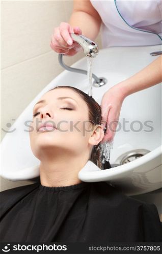 Hairstylist hairdresser washing customer hair. Brunette girl young woman relaxing in hairdressing beauty salon.