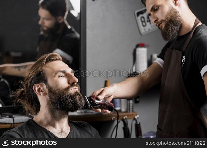 hairstylist trimming male client s hair with electric trimmer