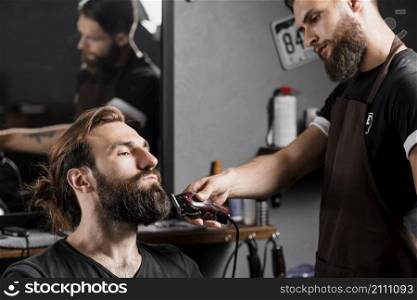 hairstylist trimming male client s hair with electric trimmer