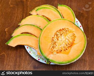 half and slices of ripe sicilian muskmelon (cantaloupe melon) on plateon wooden table