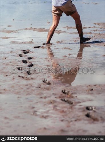 Half body shot of man walking in mud land left footprints behind. Mangrove forest area excursion in Thailand