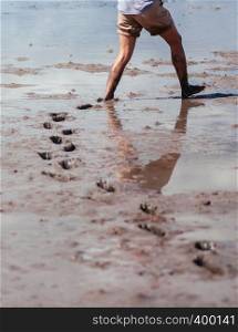 Half body shot of man walking in mud land left footprints behind. Mangrove forest area excursion in Thailand