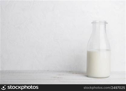 Half empty glass bottle of milk on white wooden table background with copy space