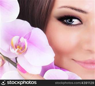 Half face of gorgeous young model, beautiful woman eye with fresh pink orchid flower, part of female head, sexy girl with stylish look, spa and beauty background