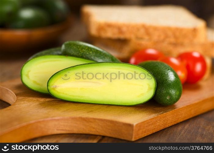 Half finger or cocktail avocado on wooden board with toast bread slices and cherry tomatoes in the back (Selective Focus, Focus on the the upper part of the avocado half )
