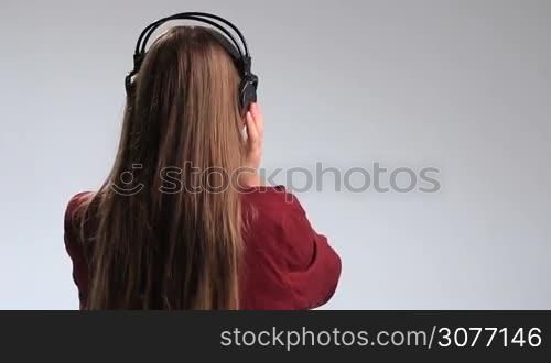Half-lenght of young charming brunette woman with beautiful long hair listening to music with massive earohones on her head rear view. Stunning girl turning back and smiling happily at camera while enjoying the track on the radio.