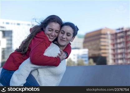 Half length of two blonde and redhead women friends having fun outdoor in the city, riding piggyback - happiness, friendship, having fun concept