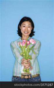 Half length portrait of pretty Asian mid adult woman holding flowers on blue background.