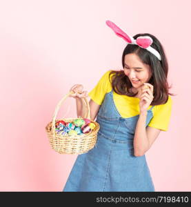 Half length studio shot of asian beauty happy young woman wearing bunny ears and holding colorful Easter egg in wood basket with lovely smile and colorful decor costume isolated on pastel backgrounds.