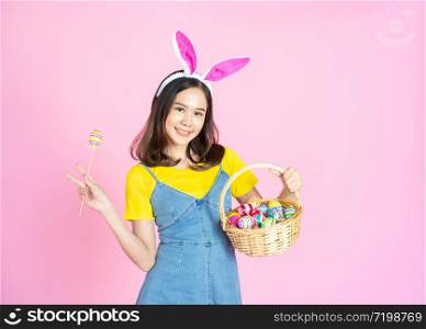 Half length studio shot of asian beauty happy young woman wearing bunny ears and holding colorful Easter egg in wood basket with lovely smile and colorful decor costume isolated on pastel backgrounds.