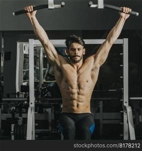 Half-naked young man doing pull ups in the gym