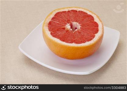 half of red grapefruit on white square bowl against tablecloth