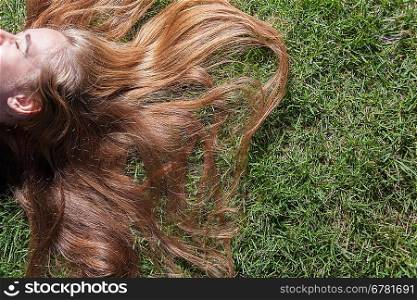 Half of the face of blonde, a lot of copyspace composition. Woman relaxes on the grass. Cute young female lying on grass field at the park.