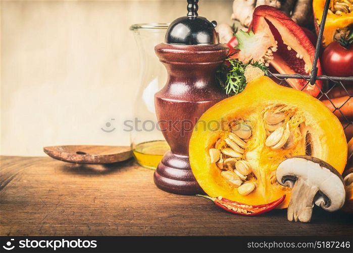 Half pumpkin with seeds, and other vegetarian ingredients on wooden kitchen table, front view. Healthy autumn seasonal cooking and eating