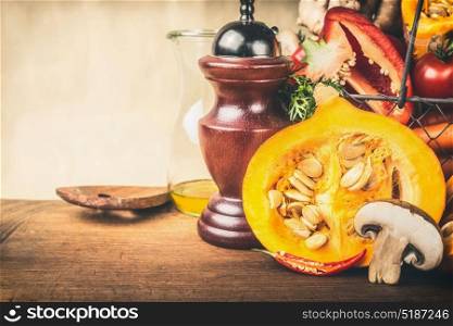 Half pumpkin with seeds, and other vegetarian ingredients on wooden kitchen table, front view. Healthy autumn seasonal cooking and eating