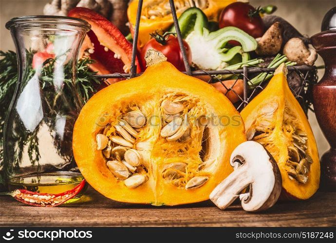 Half pumpkin with seeds, and other vegetarian ingredients on wooden table, front view. Healthy autumn seasonal cooking and eating