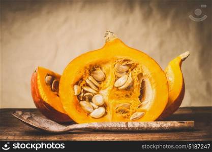 Half pumpkin with seeds and wooden cooking spoon at natural beige background, front view. Healthy autumn seasonal food and eating