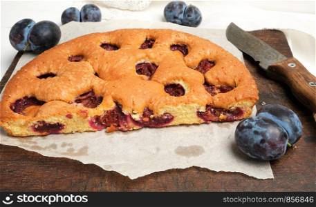 half sponge plum cake on parchment paper and knife, top view