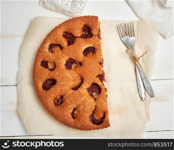 half sponge plum cake on parchment paper and two forks, top view