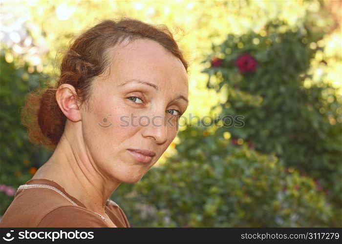 Half-turn woman portrait on the flower garden background in a fine summer day