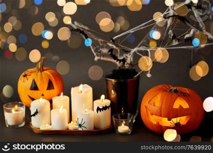 halloween and holiday concept - jack-o-lantern or carved pumpkin, burning candles and spider web decoration over bokeh lights. pumpkins, candles and halloween decorations