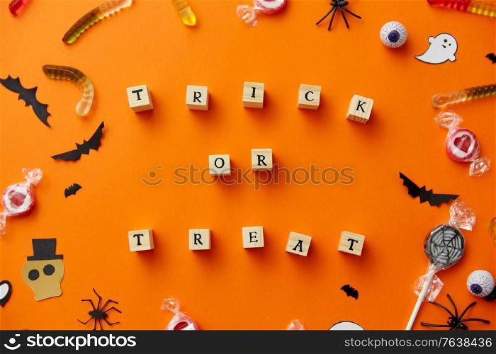 halloween and holiday concept - wooden toy blocks with trick or treat lettering candies and decorations on orange background. trick or treat letters and halloween sweets