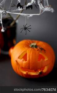 halloween and holiday decorations concept - jack-o-lantern or carved pumpkin and spiders on spiderweb. pumpkins, candles and halloween decorations