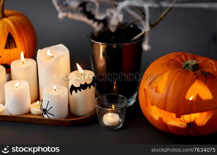 halloween and holiday decorations concept - jack-o-lantern or carved pumpkin, burning candles, spiders and bats on spiderweb. pumpkins, candles and halloween decorations
