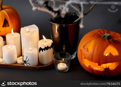 halloween and holiday decorations concept - jack-o-lantern or carved pumpkin, burning candles, spiders and bats on spiderweb. pumpkins, candles and halloween decorations