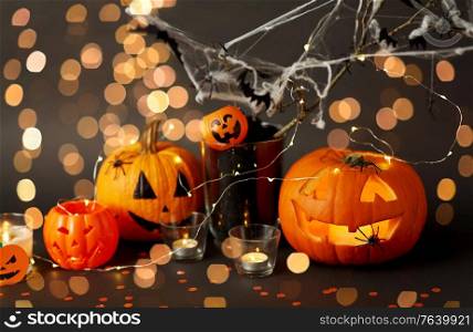 halloween and holiday decorations concept - jack-o-lantern or carved pumpkin, burning candles, electric garland string and bats on spider web over bokeh lights. pumpkins, candles and halloween decorations