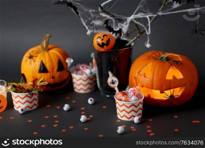 halloween and holiday decorations concept - jack-o-lantern or carved pumpkin, candies in paper cups and spiders. pumpkins, candies and halloween decorations
