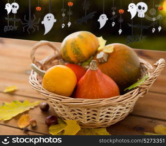 halloween and holidays - pumpkins in wicker basket with leaves on wooden table and paper party decorations over dark background. pumpkins in basket and halloween party garland