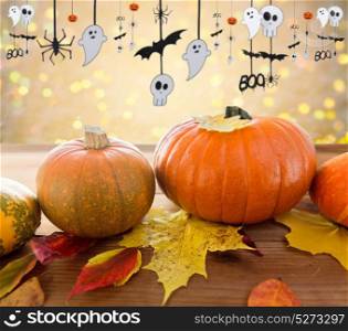 halloween and holidays - pumpkins with autumn leaves on wooden table and paper party decorations over festive lights background. pumpkins with autumn leaves and halloween garland