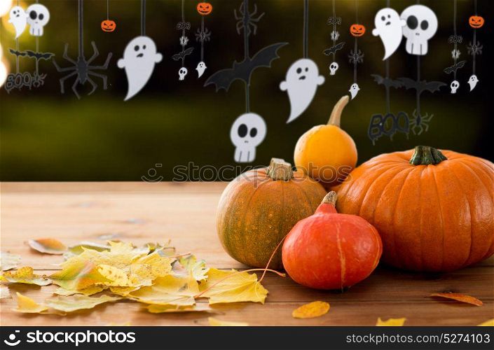 halloween and holidays - pumpkins with autumn leaves on wooden table and paper party decorations over dark background. pumpkins with autumn leaves and halloween garland