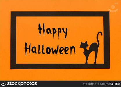 Halloween background. Black paper cat and text Happy Halloween in black frame on orange background, Halloween concept. Top view Flat lay. Halloween background. Black paper cat text Happy Halloween in black frame on orange background
