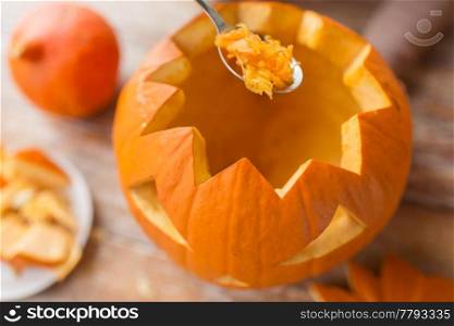 halloween, decoration and holidays concept - close up of spoon carving pumpkin flesh and making jack-o-lantern at home. close up of spoon carving halloween pumpkin