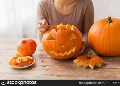 halloween, decoration and holidays concept - close up of woman with spoon carving pumpkin flesh and making or jack-o-lantern at home. close up of woman carving halloween pumpkin