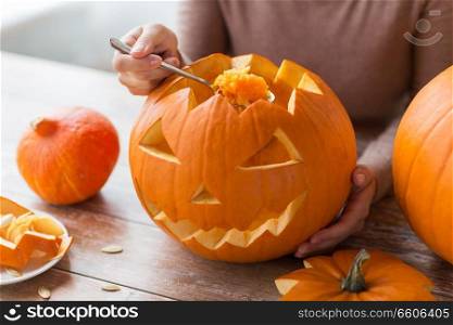 halloween, decoration and holidays concept - close up of woman with spoon carving pumpkin flesh and making or jack-o-lantern at home. close up of woman carving halloween pumpkin