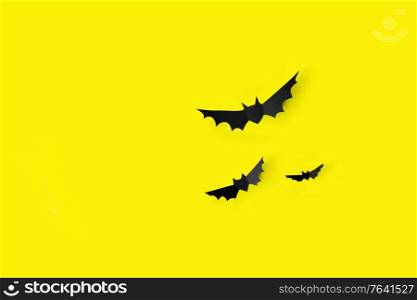 halloween, decoration and scary concept - flock of black paper bats flying over yellow background. flock of black paper bats over yellow background